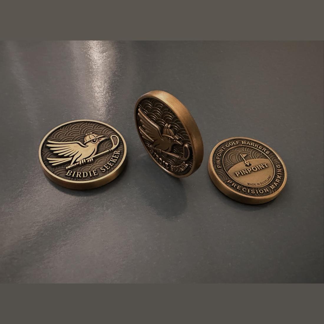 Three Birdie Seeker markers on a bench, showing the front, the edge and the back